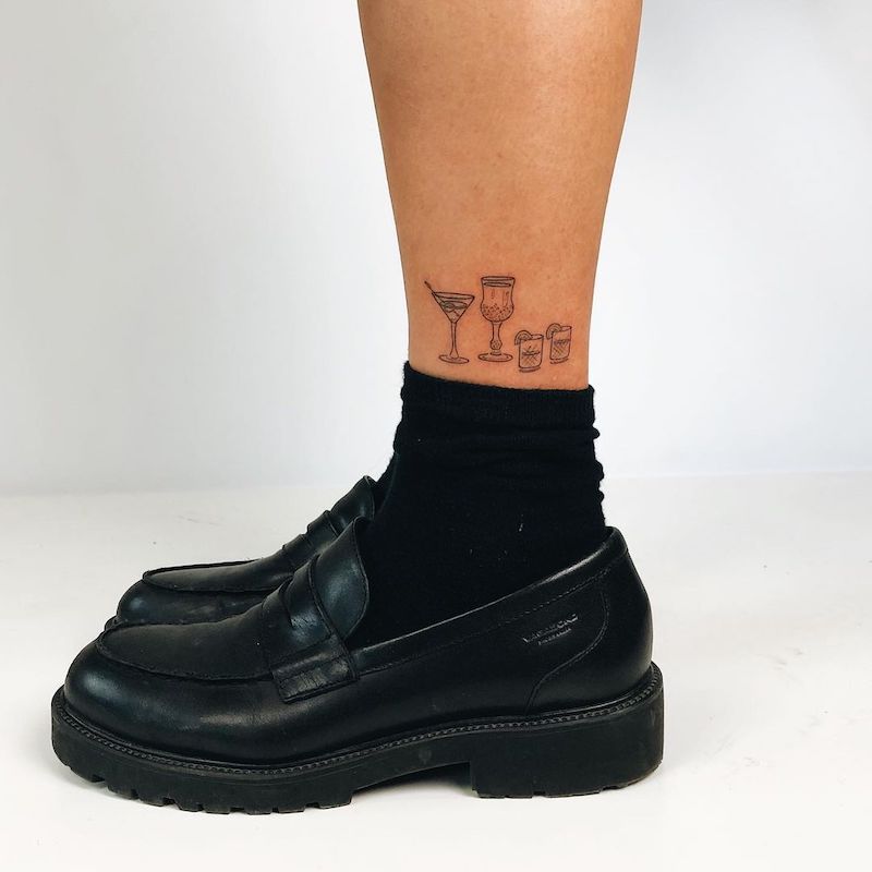 Close-up of lower leg with black loafers, socks, and four cocktails ankle tattoo