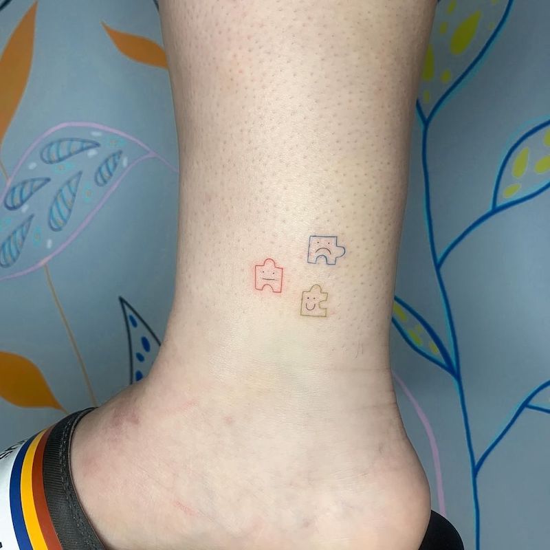 Multicolored puzzle pieces with faces ankle tattoo