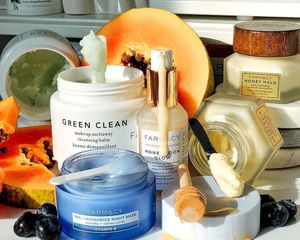 Various Farmacy products on a counter with papaya, blueberries, and honey