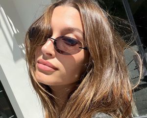 Hailey Bieber with shiny, silky brown hair and frameless sunglasses in sunlight
