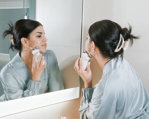 Woman using NuFace microcurrent device on face in mirror