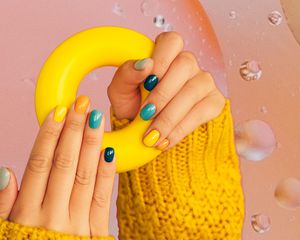 Photo composite of a woman holding a rubber ring, showing off their multi-colored manicure.