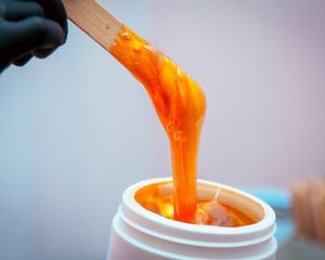 Someone pulling sugaring paste out of the jar with a stick