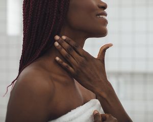 Woman with a deep skin tone applies skincare products to her neck.