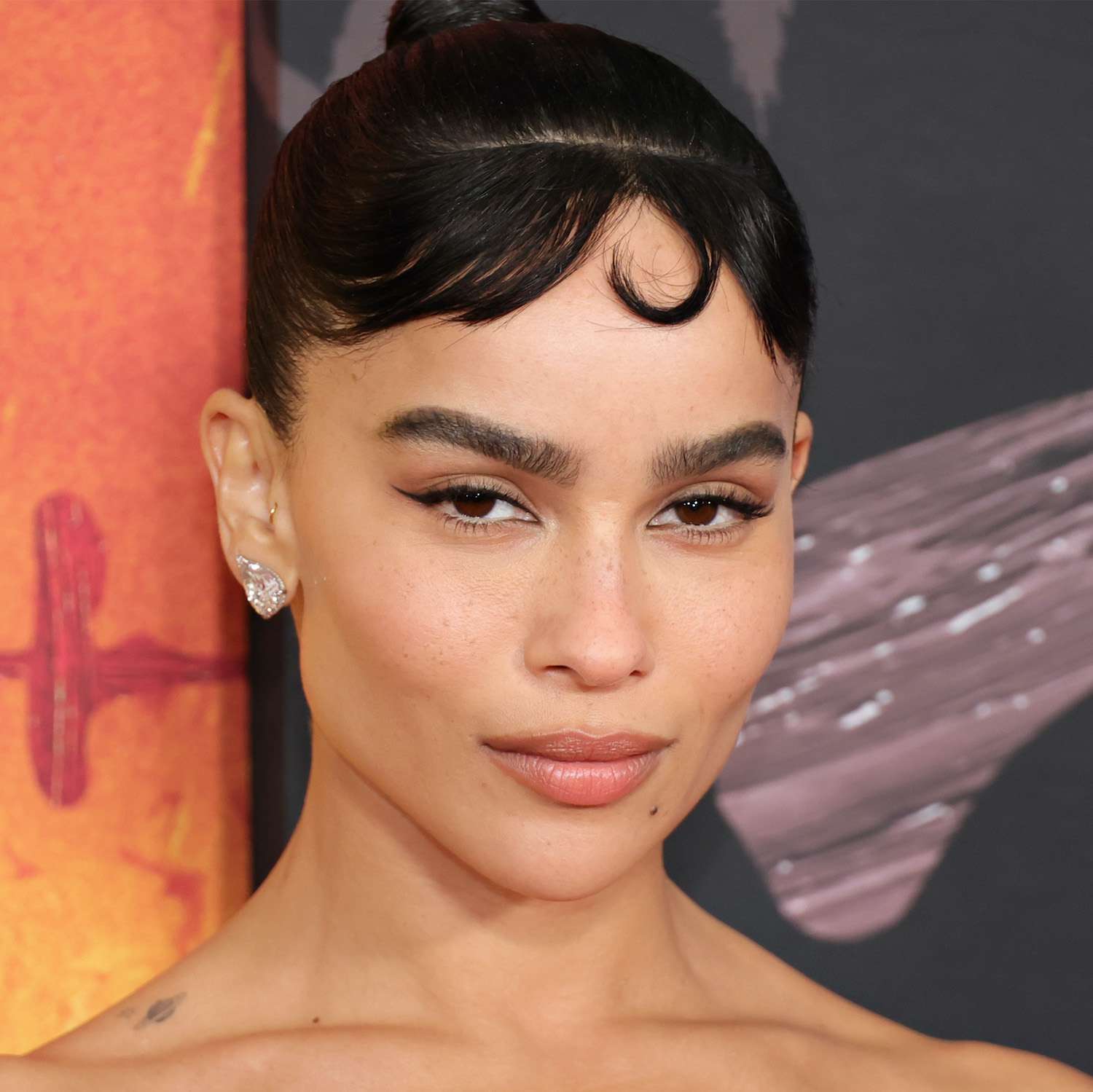 Zoe Kravitz wears an updo with baby bangs with a centered single pin curl