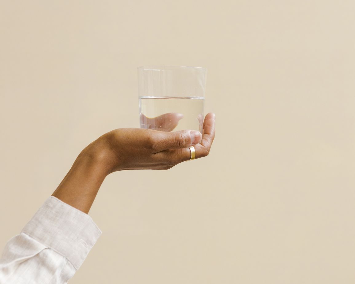 Hand holding a glass of water against a tan background.