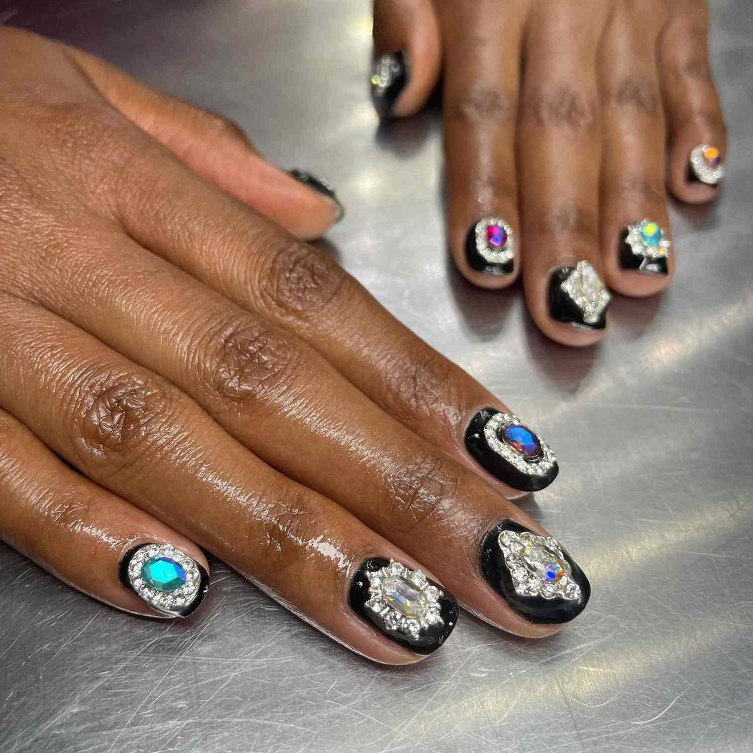 Hands with black nails studded with gemstones.