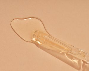 Close up of a dropper with pale yellow liquid on a blush background.