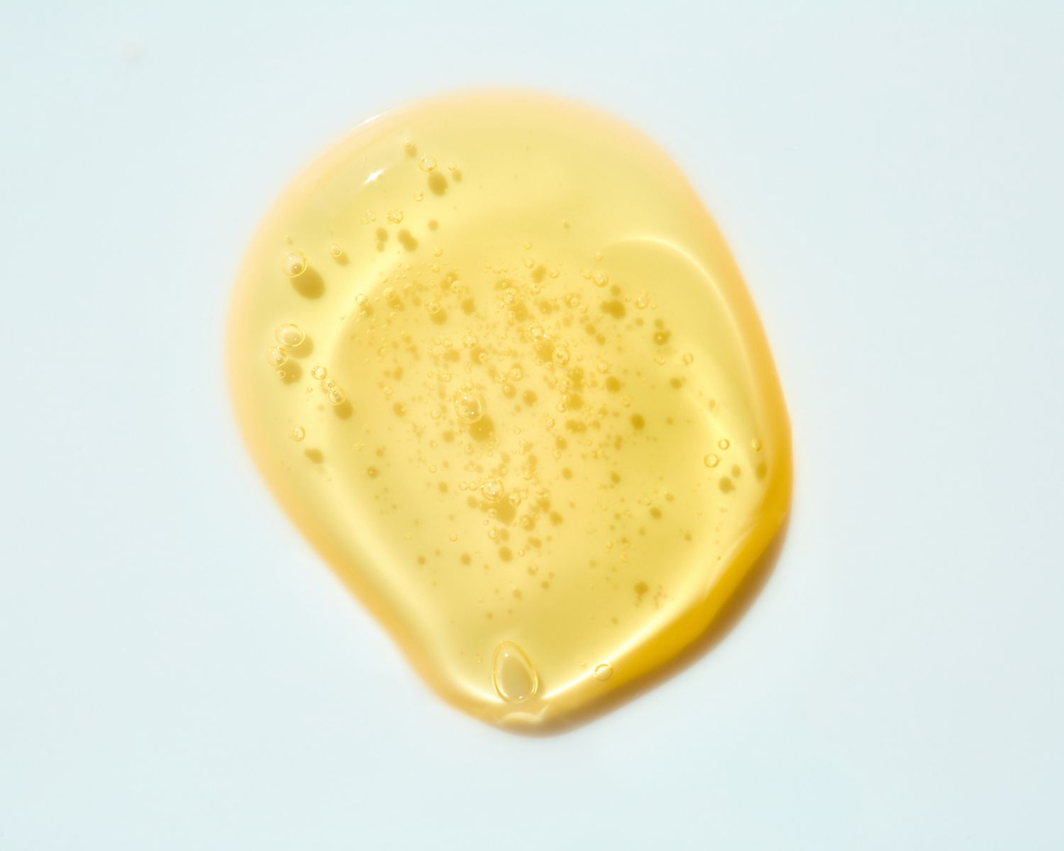 Drop of yellow-toned oil/serum texture on gray background