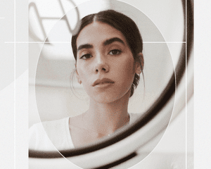 Portrait of a Woman Looking at Her Reflection in a Mirror with Minimal, Classic Makeup in a Loose Low Bun 